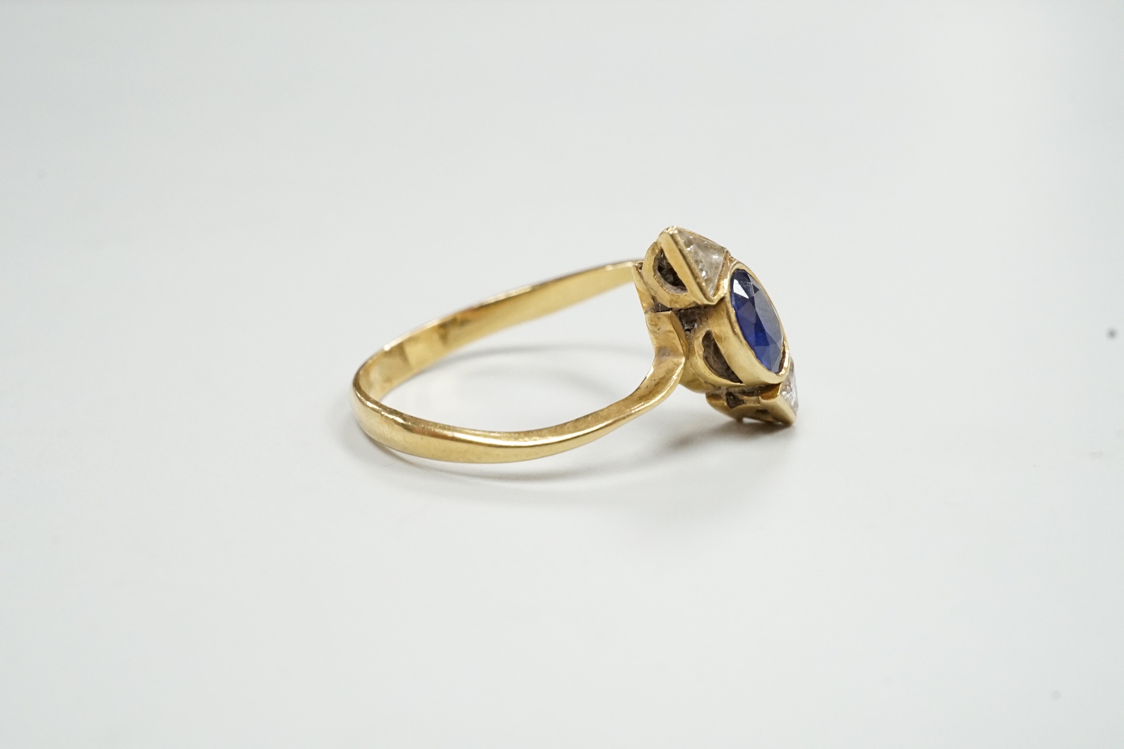 A yellow metal and single stone oval cut sapphire and two stone triangular cut diamond set ring, size L/M, gross weight 2.4 grams.